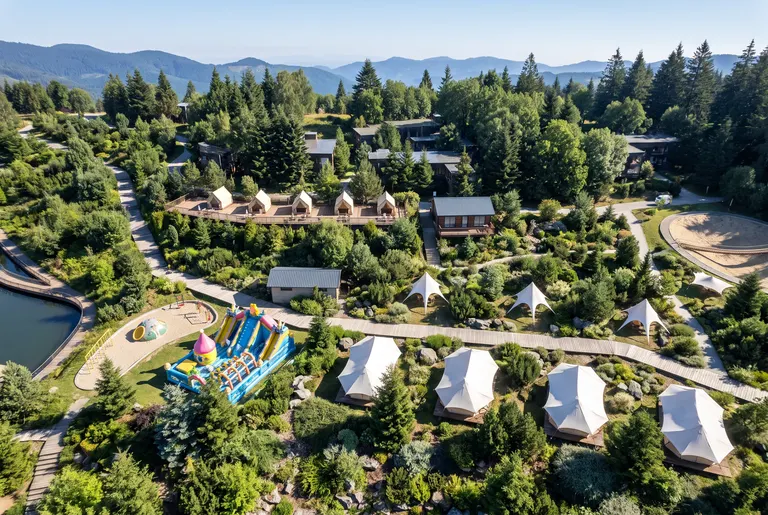 保留图1@图片1 的完整结构及视角保持不变，添加自然山林配景，贴合现有起伏的绿色山坡地形，营造原生山林氛围，在山坡上自然分布各类原生常绿乔木与灌木，以深浅不一的